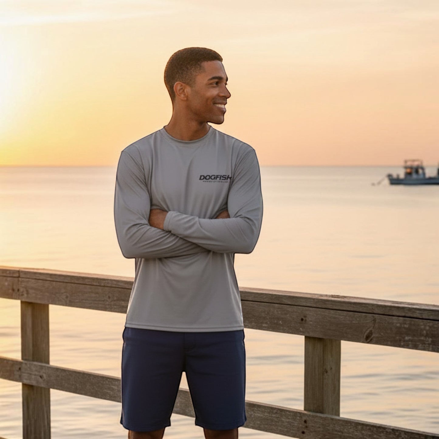 Man wearing a gray long-sleeve shirt with 'Dogfish' logo by the ocean at sunset.