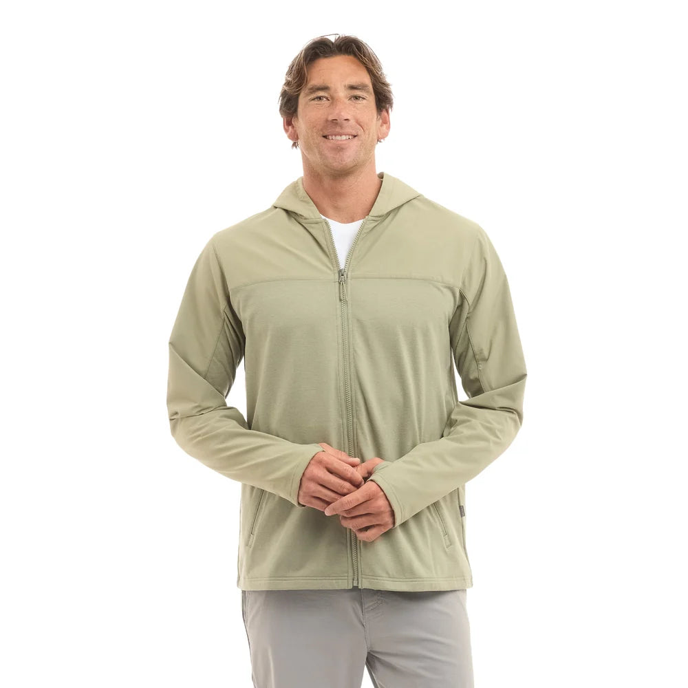 A man wearing a light sage green zip-up hooded jacket over a white t-shirt and gray pants, standing against a solid white background.