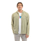 A man wearing a light sage green hooded zip-up jacket over a white graphic t-shirt and gray pants, standing against a plain white background.