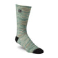 A single crew sock with a sage green and beige wavy pattern, featuring solid black heels, toes, and a small black brand patch near the cuff, shown on a white background.