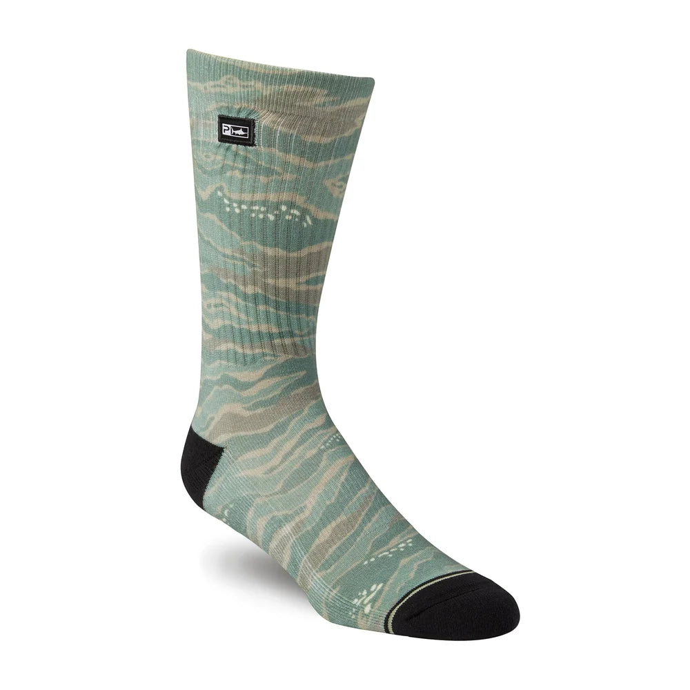 A single crew sock with a sage green and beige wavy pattern, featuring solid black heels, toes, and a small black brand patch near the cuff, shown on a white background.