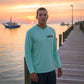 Man wearing a light blue hoodie with a logo on a dock at sunset