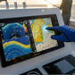 Dogfish Tackle & Marine blue Aftco utility fishing glove touching a boat's touchscreen marine navigation display