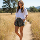 Dogfish Tackle & Marine women wearing camo Prime Hagood shorts with a white top on a sunny outdoor trail