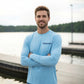 Dogfish Tackle & Marine light blue microfiber long sleeve shirt with logo. Model wears shirt with arms crossed.