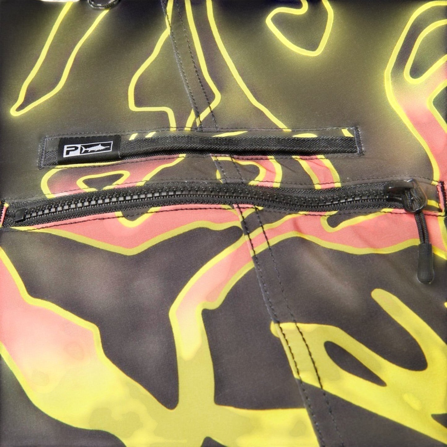 Dogfish Tackle & Marine boardshorts with a black, yellow, and pink abstract graphic print. Features a zip pocket and a logo patch.