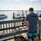Dogfish Tackle & Marine heathered navy blue t-shirt with fishing boat graphic on back, worn by man cleaning fish on dock.
