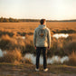 Dogfish Tackle & Marine Marsh Wear hoodie in pigment-dyed tan fleece with a back graphic standing in a marsh at sunset