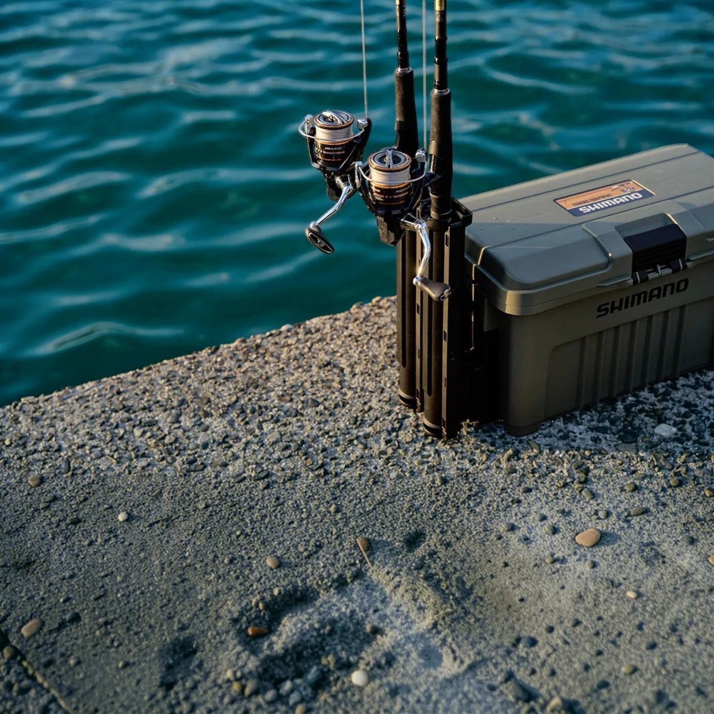 Dogfish Tackle & Marine Shimano Nexave FJ spinning reels with fishing rods and tackle box on a concrete pier by the water.