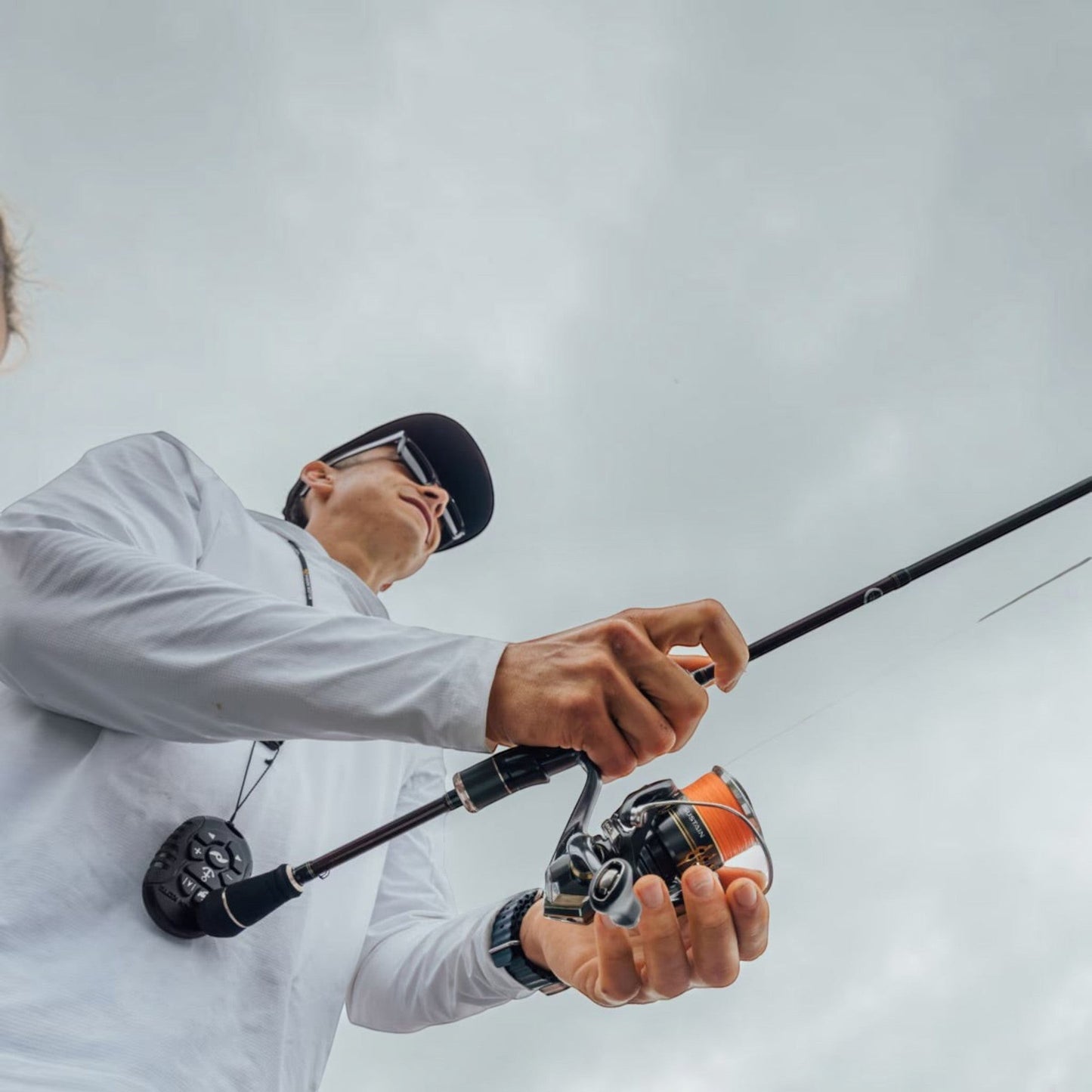 Dogfish Tackle & Marine Shimano Sustain FK spinning reel with orange spool, held by a man in a white long-sleeve shirt and black cap.