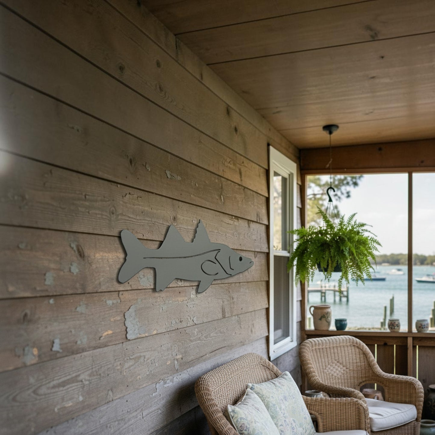 Dogfish Tackle & Marine metal fish wall art mounted on a rustic wooden porch overlooking a coastal water view.