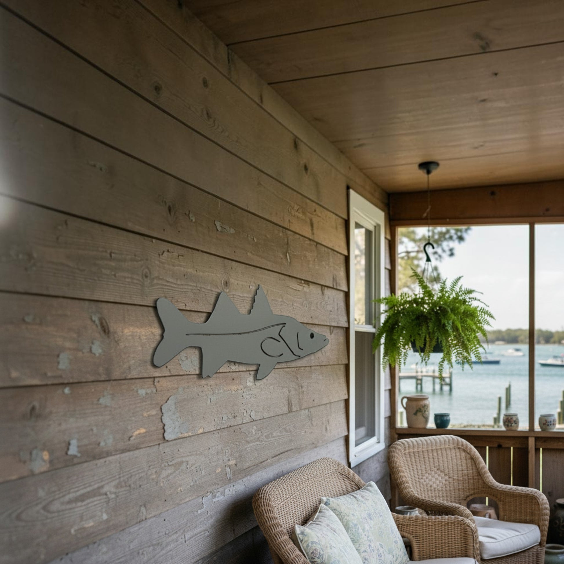 Dogfish Tackle & Marine metal fish wall art mounted on a rustic wooden porch overlooking a coastal water view.